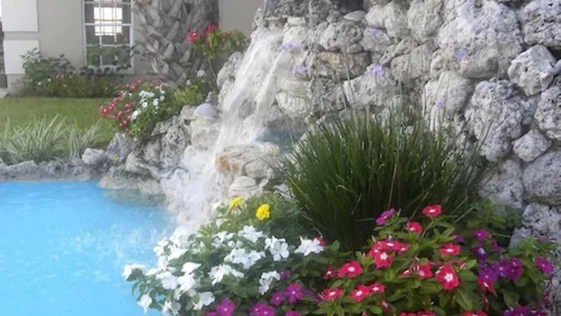 Ein Pool mit Wasserfall, umgeben von bunten Blumen und viel Grün.
