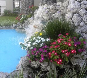 A pool with a waterfall feature surrounded by colorful flowers and greenery. - Travelodge by Wyndham Venice (Venice)