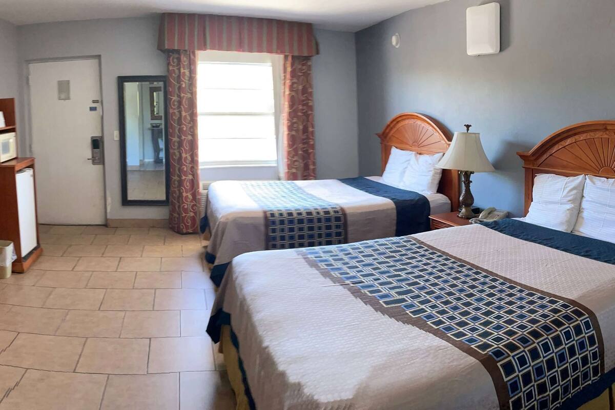Een hotelkamer met twee bedden, een bureau, een telefoon en een raam met gordijnen.