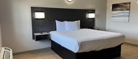 A hotel room with a large bed, two bedside tables with lamps, a wall-mounted light, and a painting on the wall.