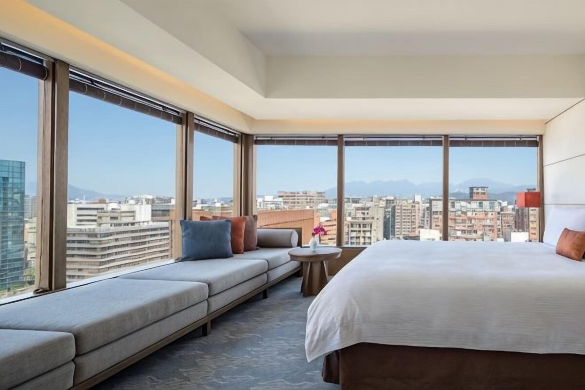 Habitación de hotel con una cama grande, un sofá, una mesita y vistas a la ciudad.