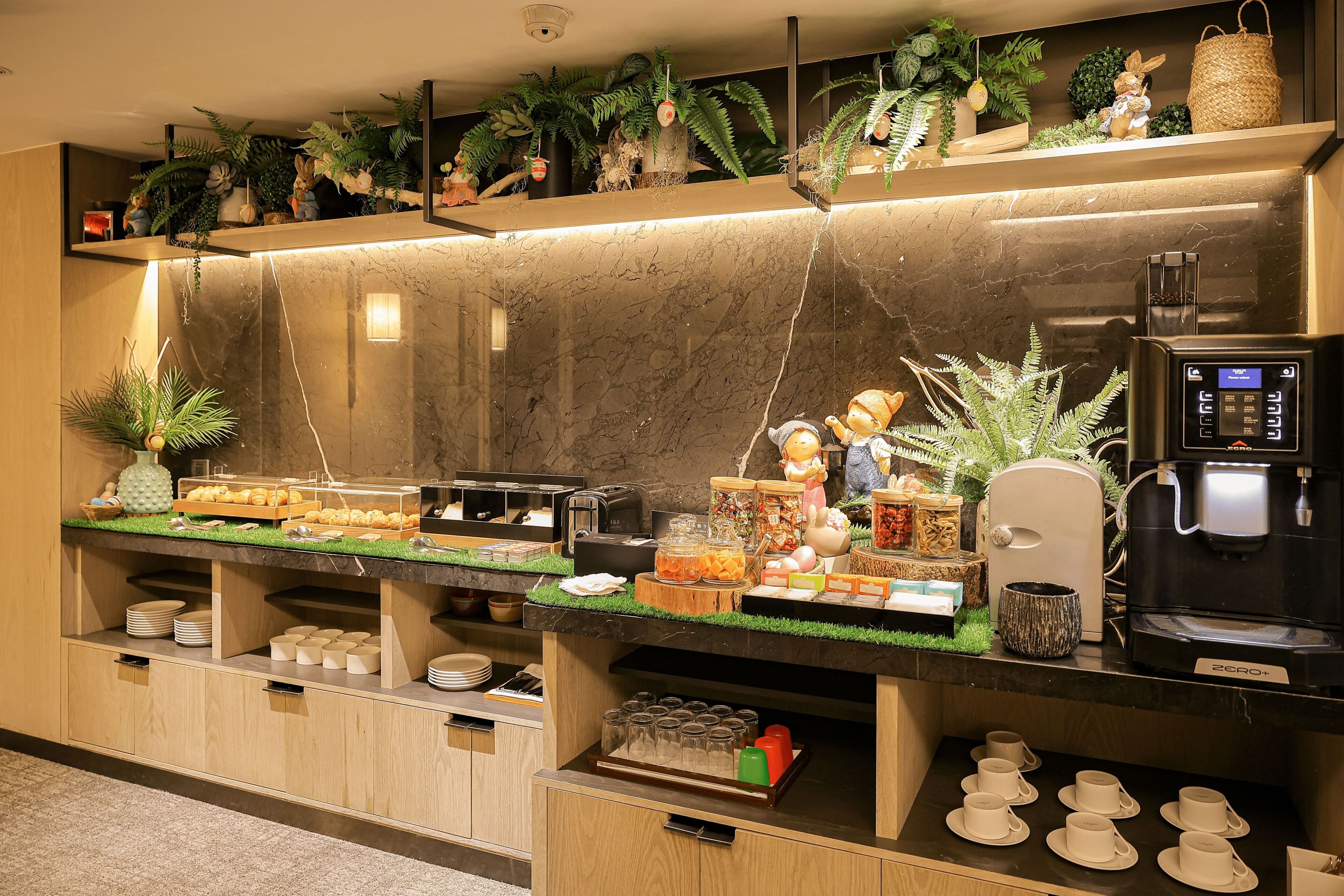 A buffet area with various food items, a coffee machine, and decorative plants.