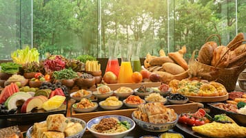 A table with a variety of dishes and beverages, set against a backdrop of a forest view through large windows.