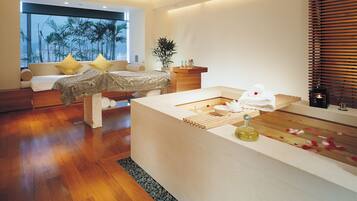 A modern bedroom with a large bed, a bedside table with toiletries, and a view of palm trees through the window.