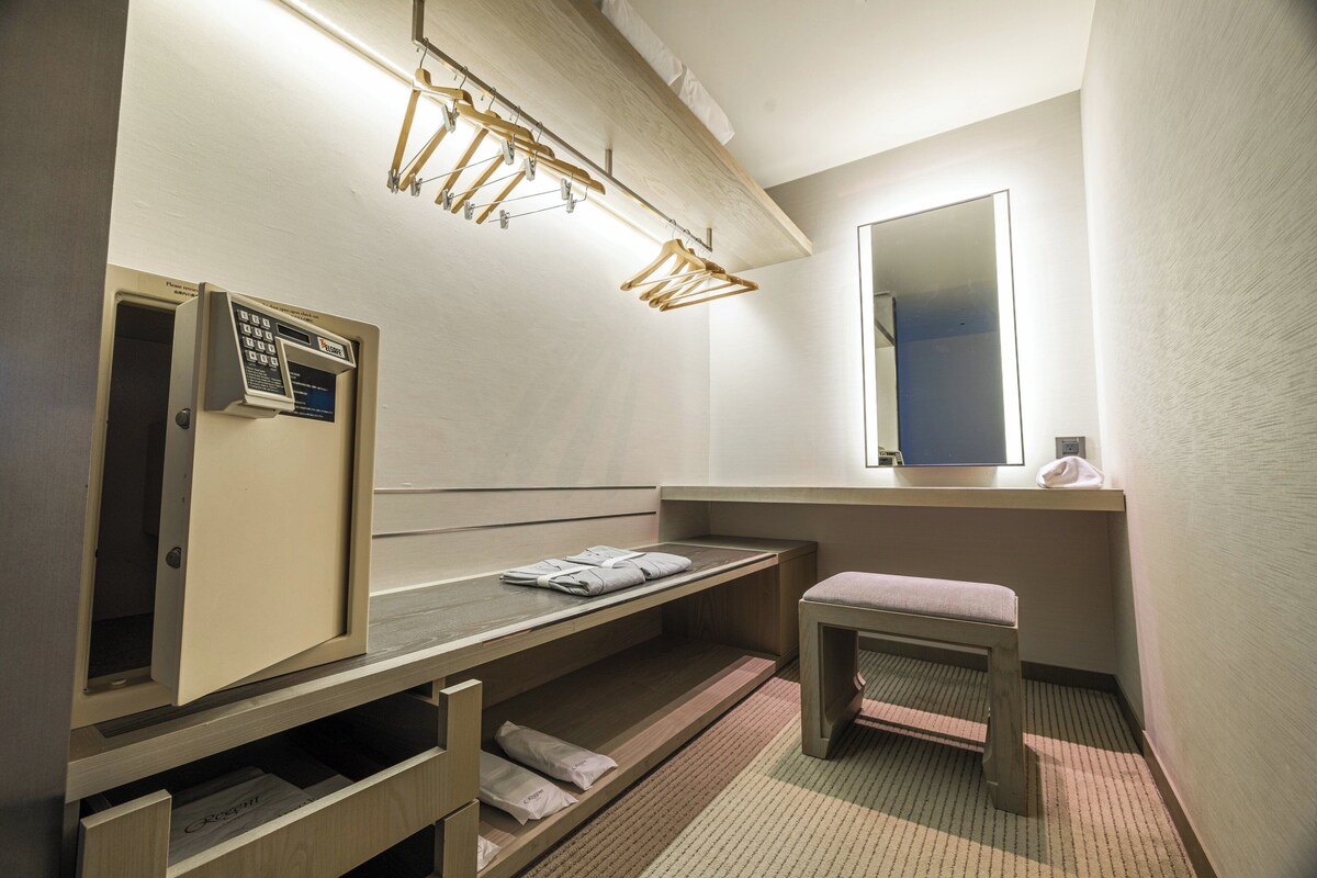 Un baño de hotel con un banco de madera, un perchero, un espejo y una zona de ducha.