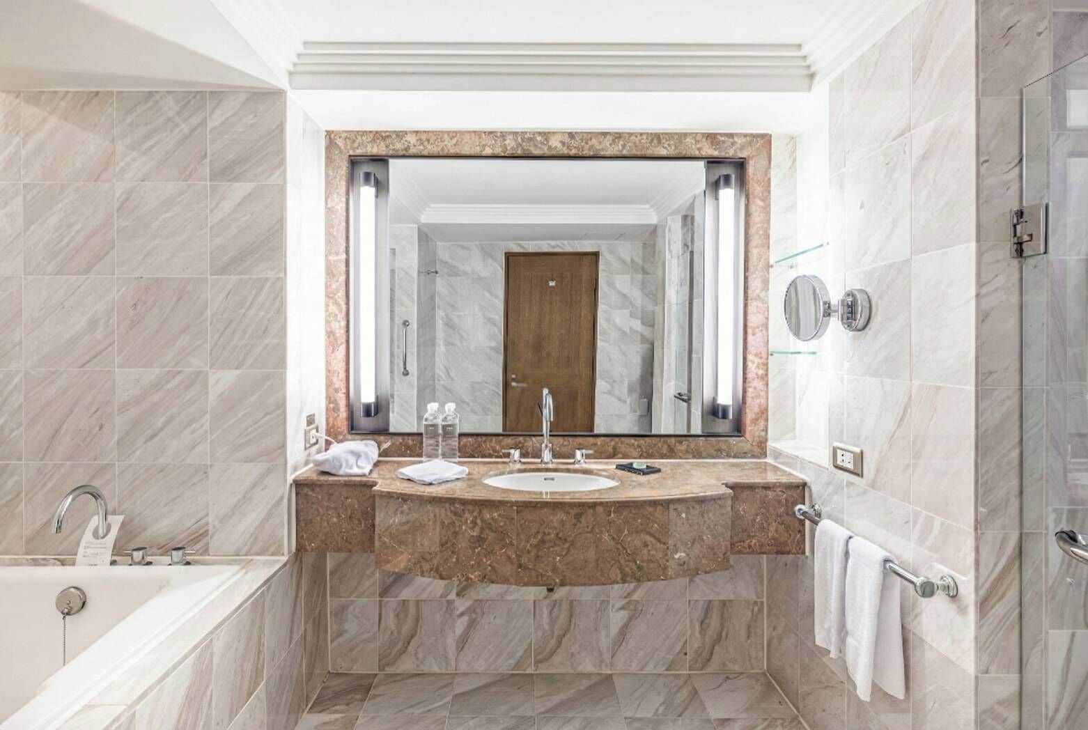 A modern bathroom with a marble vanity, a large mirror, a bathtub, and a shower area.