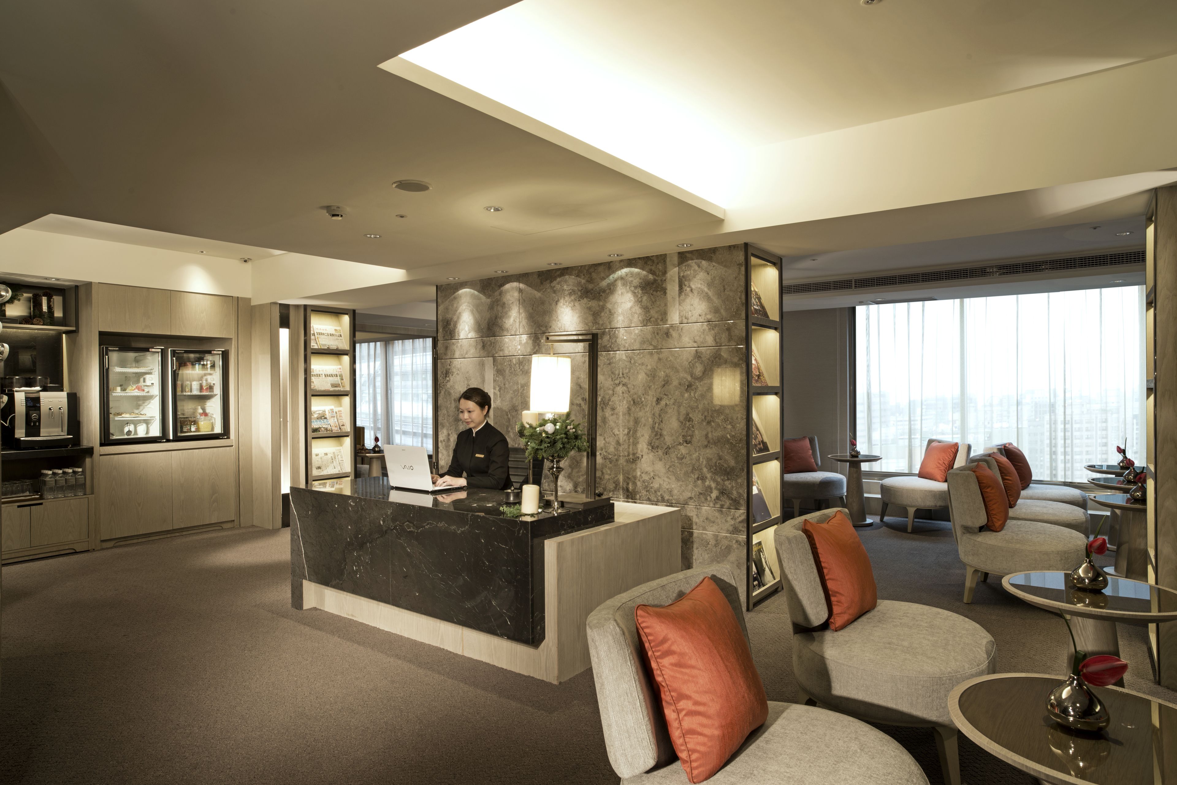 A modern hotel lobby with a reception desk, seating area, and a bar.