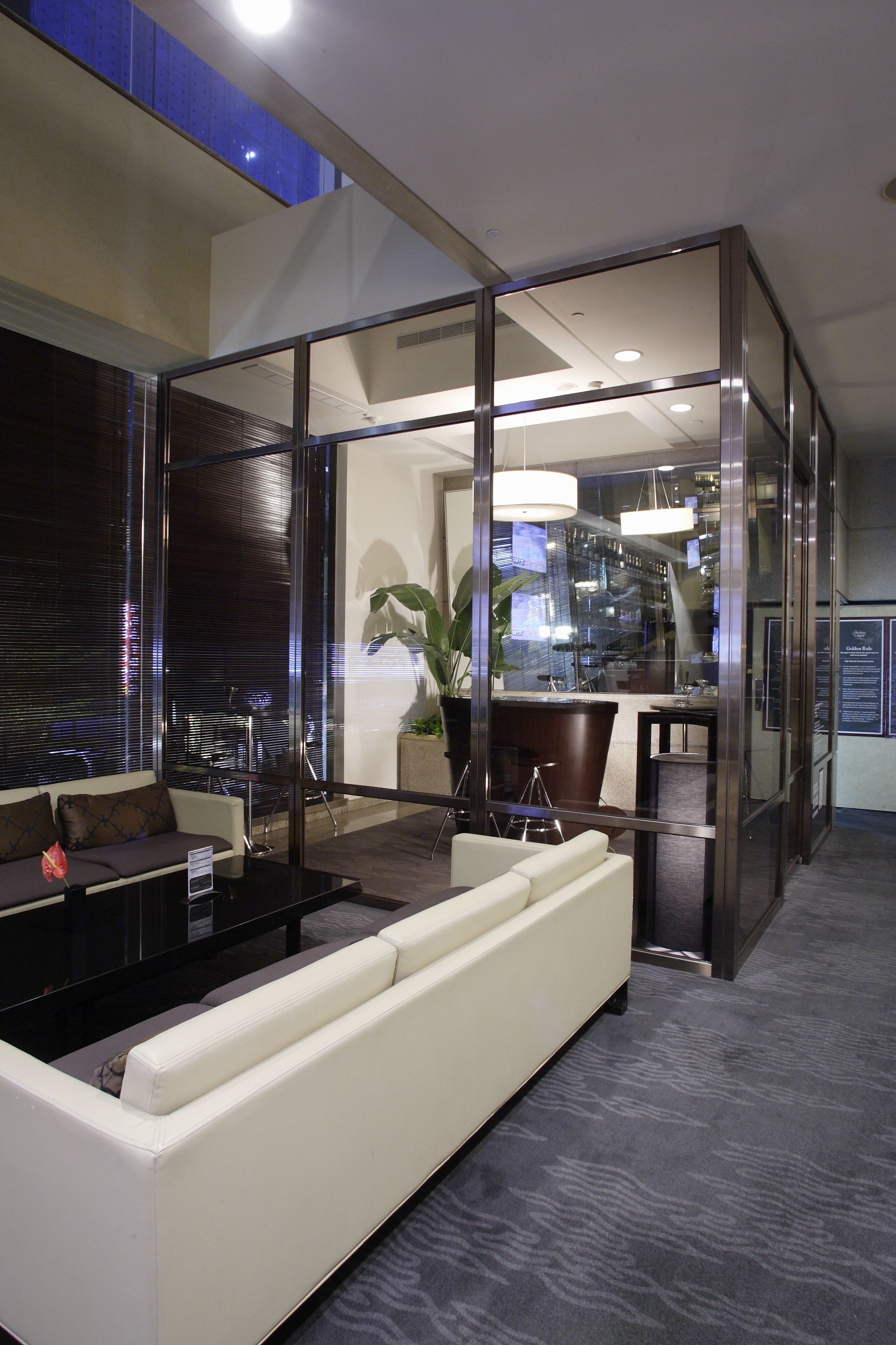 A modern hotel lobby with a white sofa, a glass partition, and a bar area.