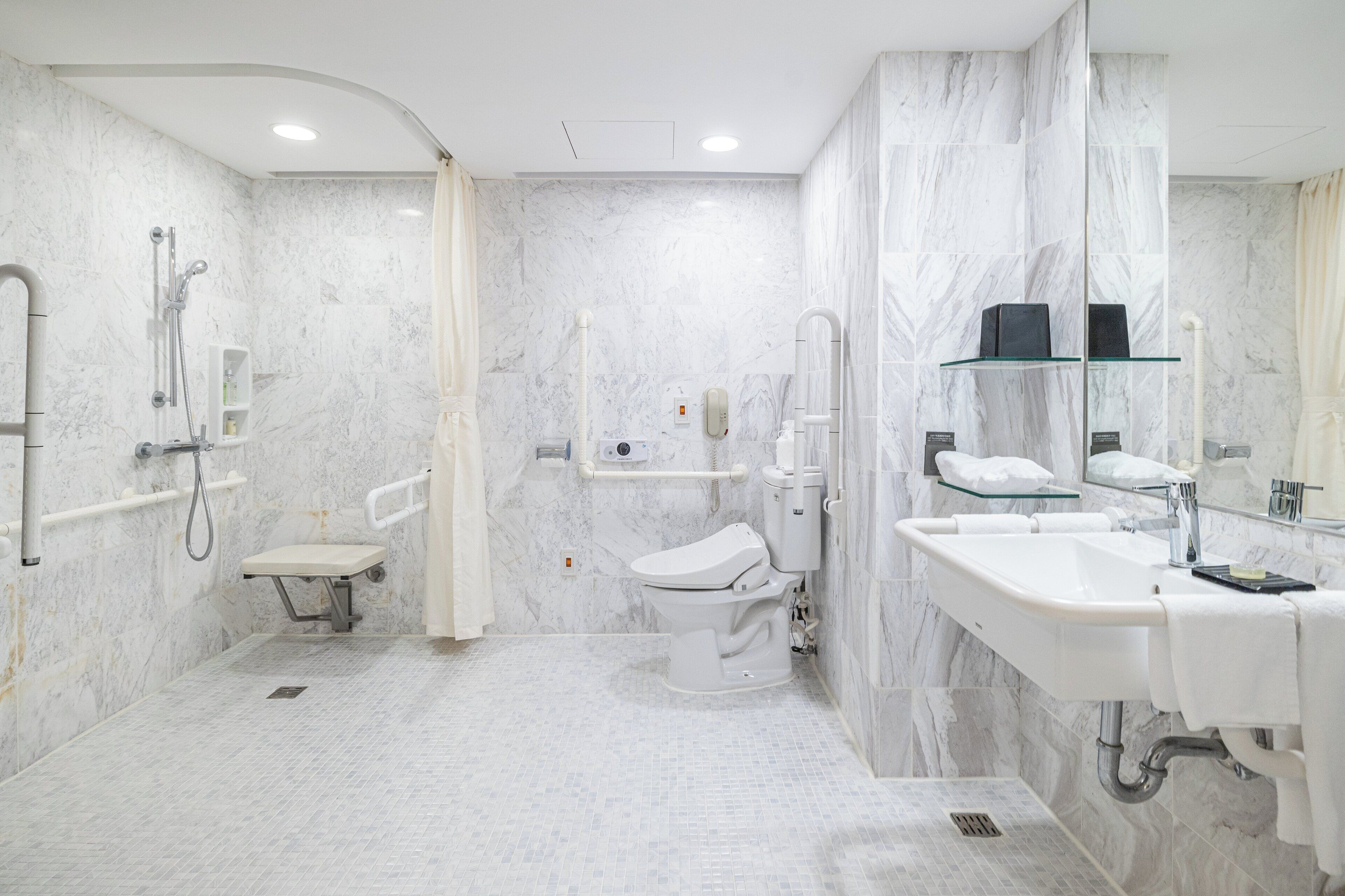 A modern bathroom with a toilet, bidet, and sink, marble walls, and a glass shelf.
