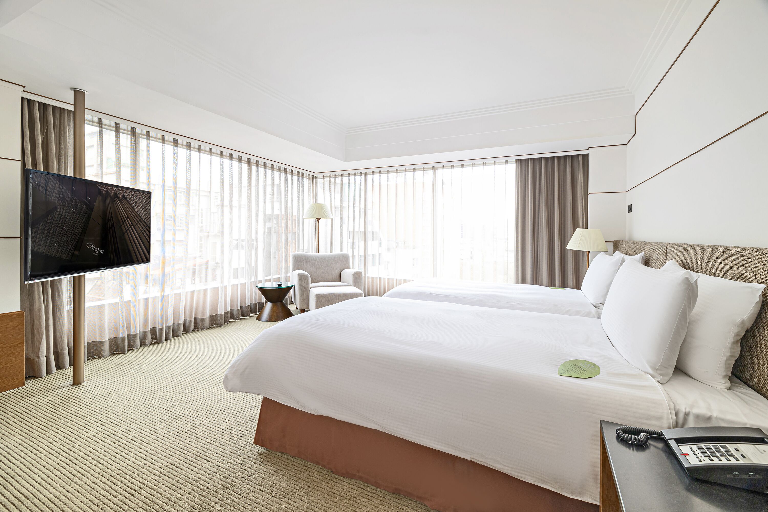 A hotel room with a large bed, a desk with a telephone, a chair, and a television.