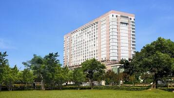 A tall, rectangular hotel with a uniform facade, surrounded by a well-maintained grassy area and trees.