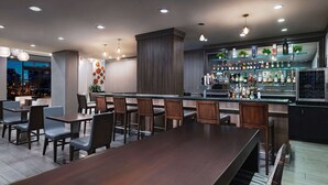 A modern bar area with a long counter, multiple seating options, and a variety of liquor bottles on shelves. - Hilton Houston Plaza/Medical Center (Houston)