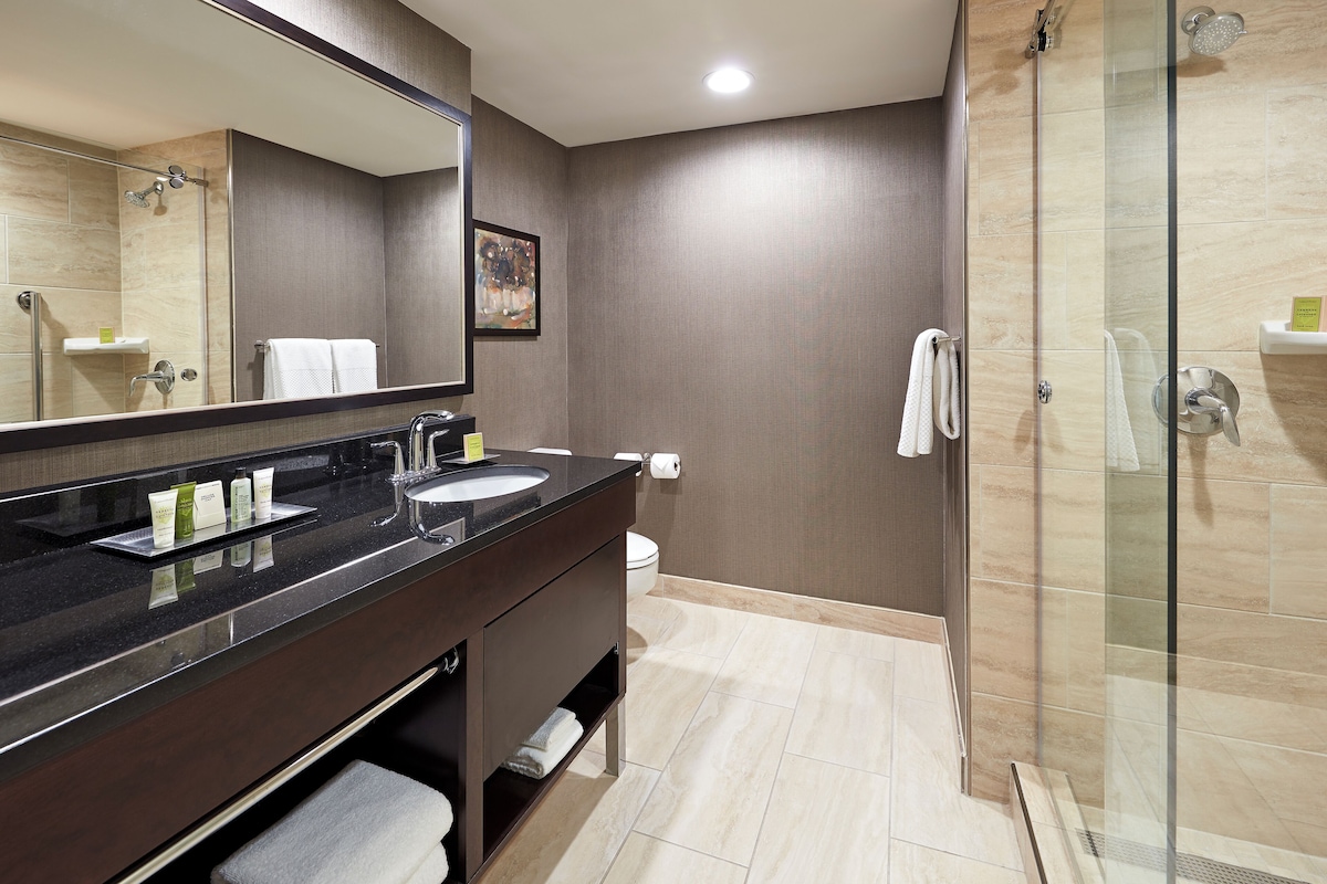A modern bathroom with a dark vanity, a glass shower enclosure, and beige tiled flooring.