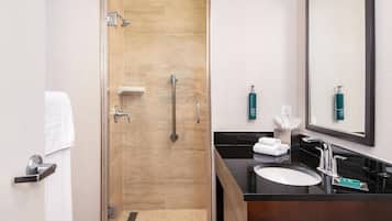 Un baño moderno con cabina de ducha de vidrio, tocador con encimera negra y un espejo grande.