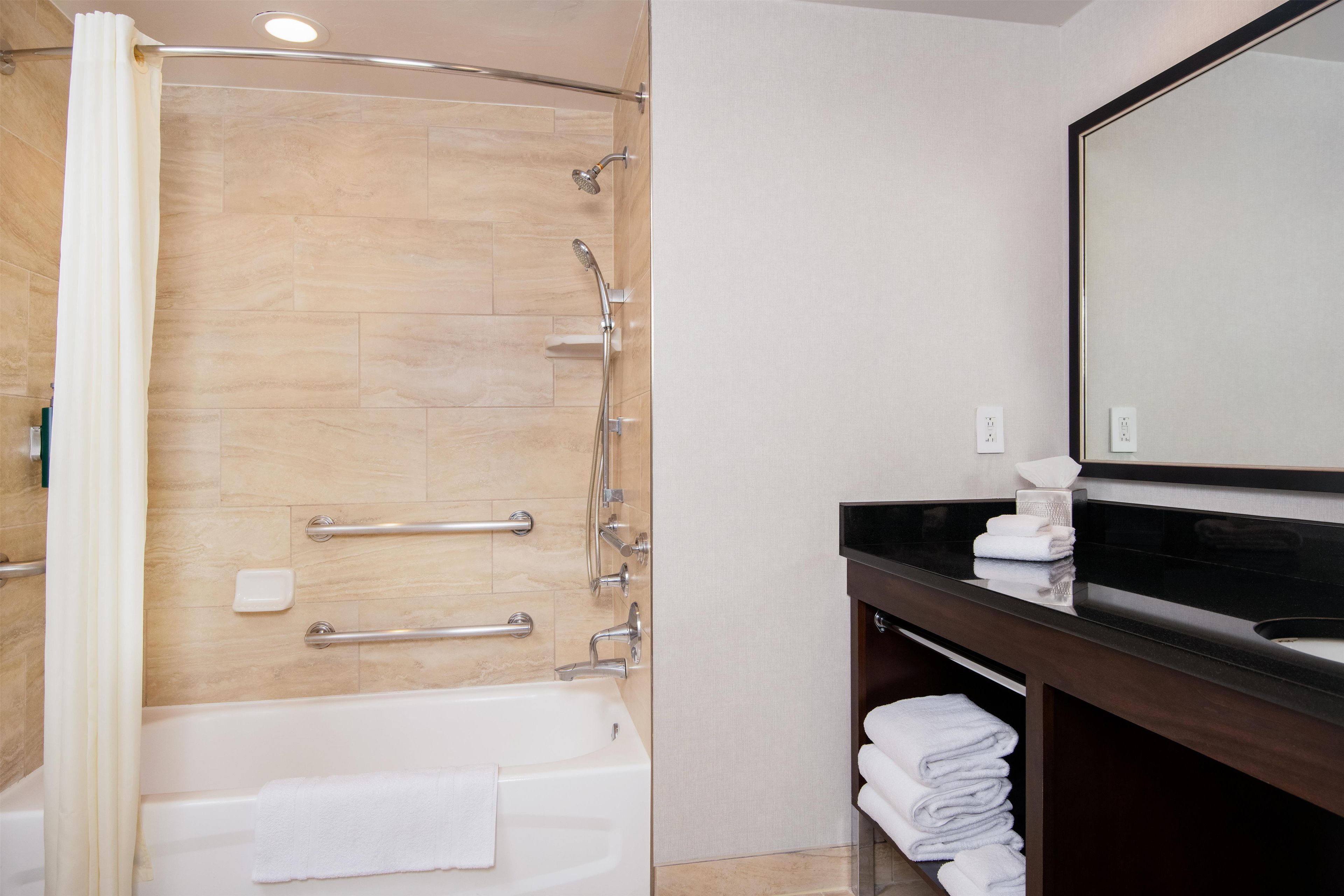 Een moderne badkamer met een bad, een douche met handdouche, een wastafel met spiegel en een handdoekrek.
