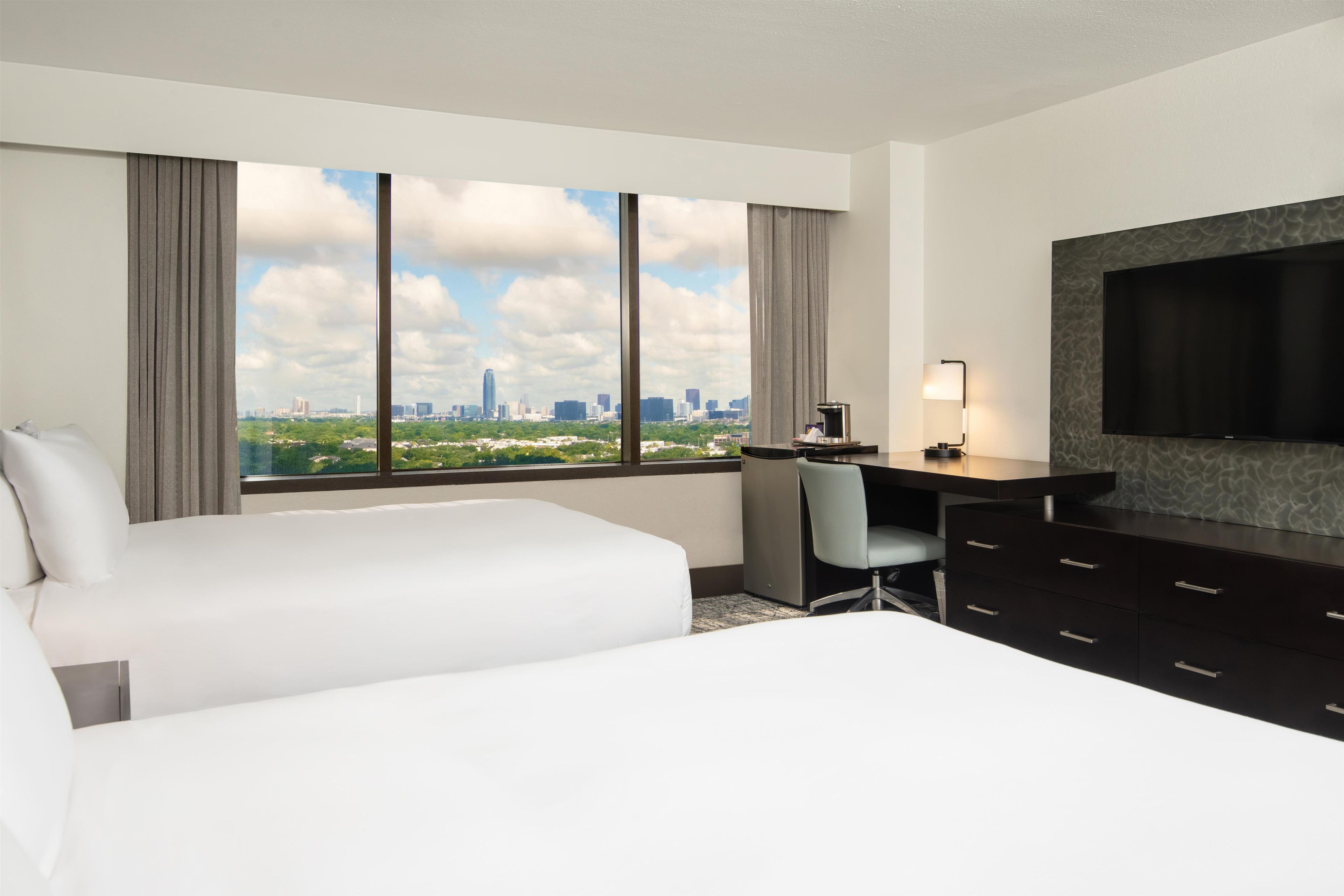 A hotel room with a bed, a desk, a chair, a coffee maker, and a TV.