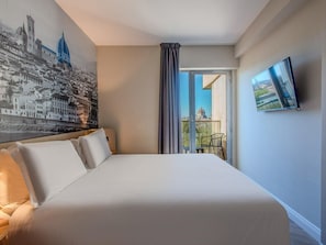 A hotel room with a large bed, a cityscape mural, a TV, and a balcony with a view of a dome and buildings.