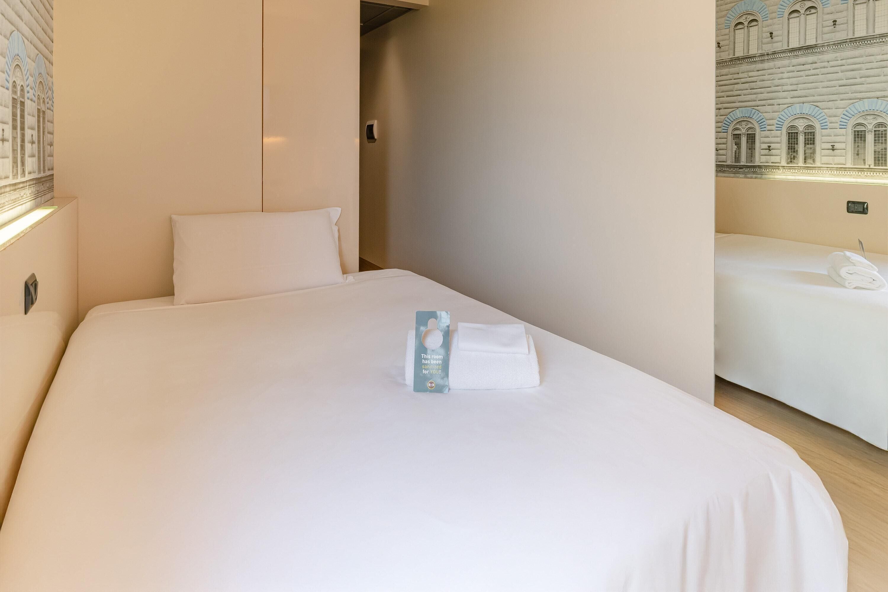 Una habitación de hotel con una cama grande, una mesita de noche pequeña y una lámpara fijada a la pared.