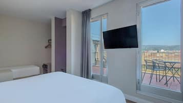 Habitación de hotel con cama, televisor montado en la pared y balcón con vistas a la ciudad.