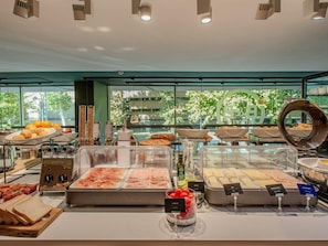 A buffet with various food options, including meats, cheeses, and fruits, with a view of trees outside.