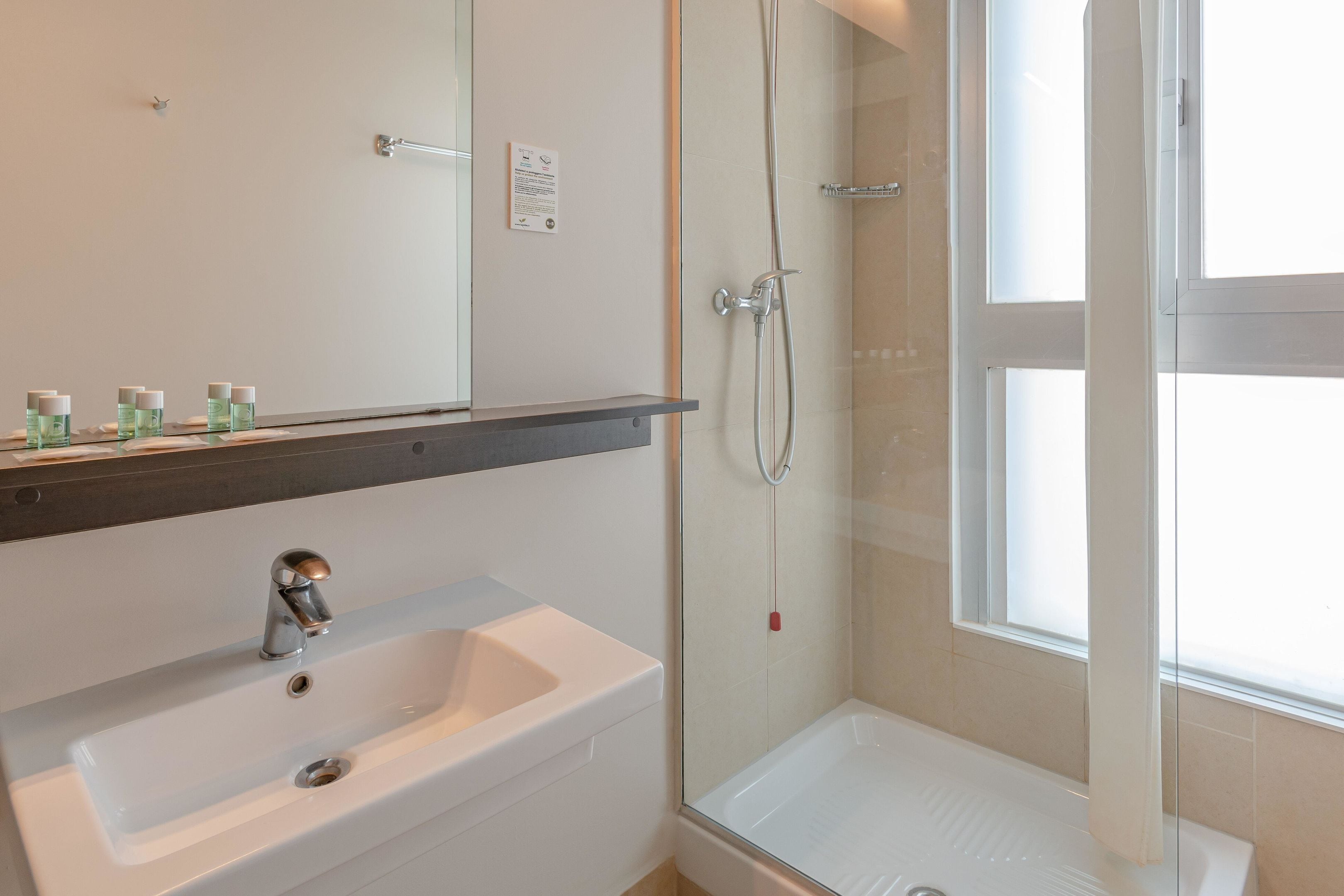 Une salle de bain moderne avec un lavabo blanc, un miroir, une cabine de douche et une fenêtre.