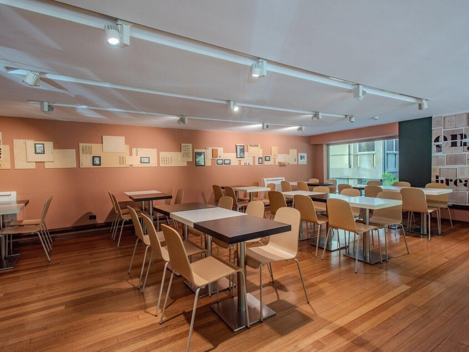 A spacious dining area with multiple tables and chairs, wooden flooring, and ceiling lights.
