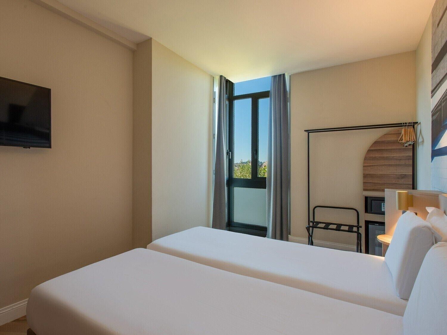 Une chambre d’hôtel avec un lit, un téléviseur fixé au mur, une fenêtre avec des rideaux et une vue sur l’extérieur.