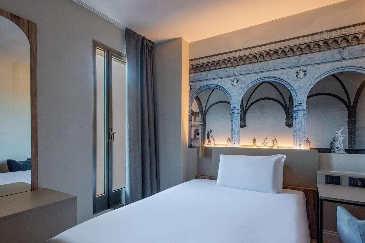 Een hotelkamer met een bed, een bureau en een grote spiegel.