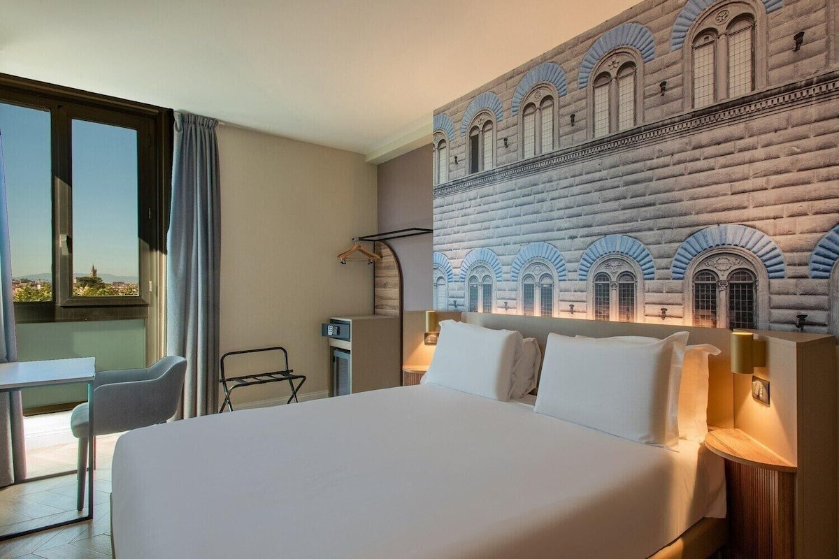 Een hotelkamer met een groot bed, een bureau en uitzicht op een gebouw.