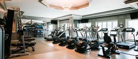 Un gimnasio con varios equipos de ejercicio, incluyendo cintas de correr, elípticas y máquinas de pesas.