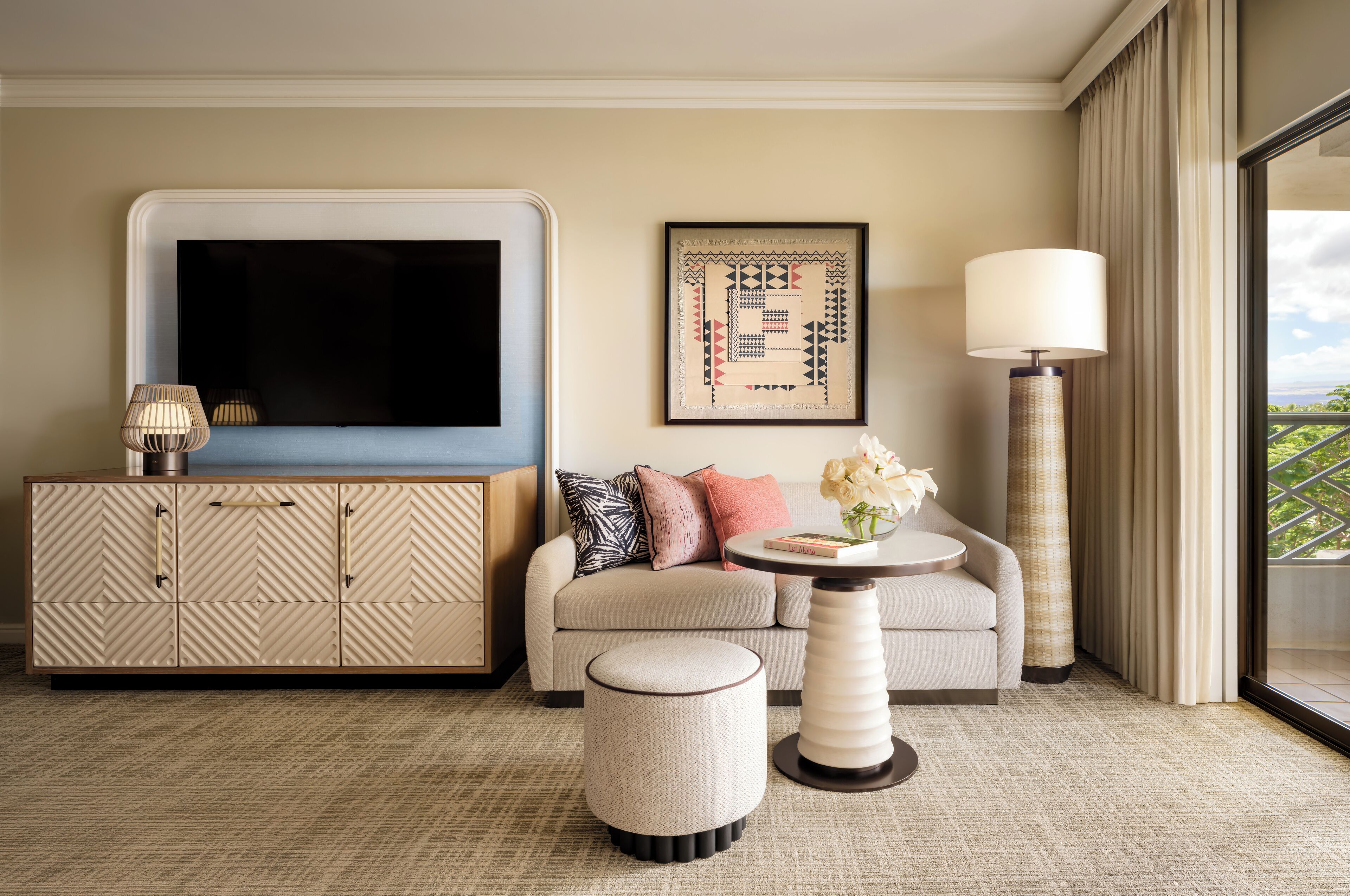 A modern living room with a sofa, ottoman, side table, and a flat-screen TV mounted on the wall.