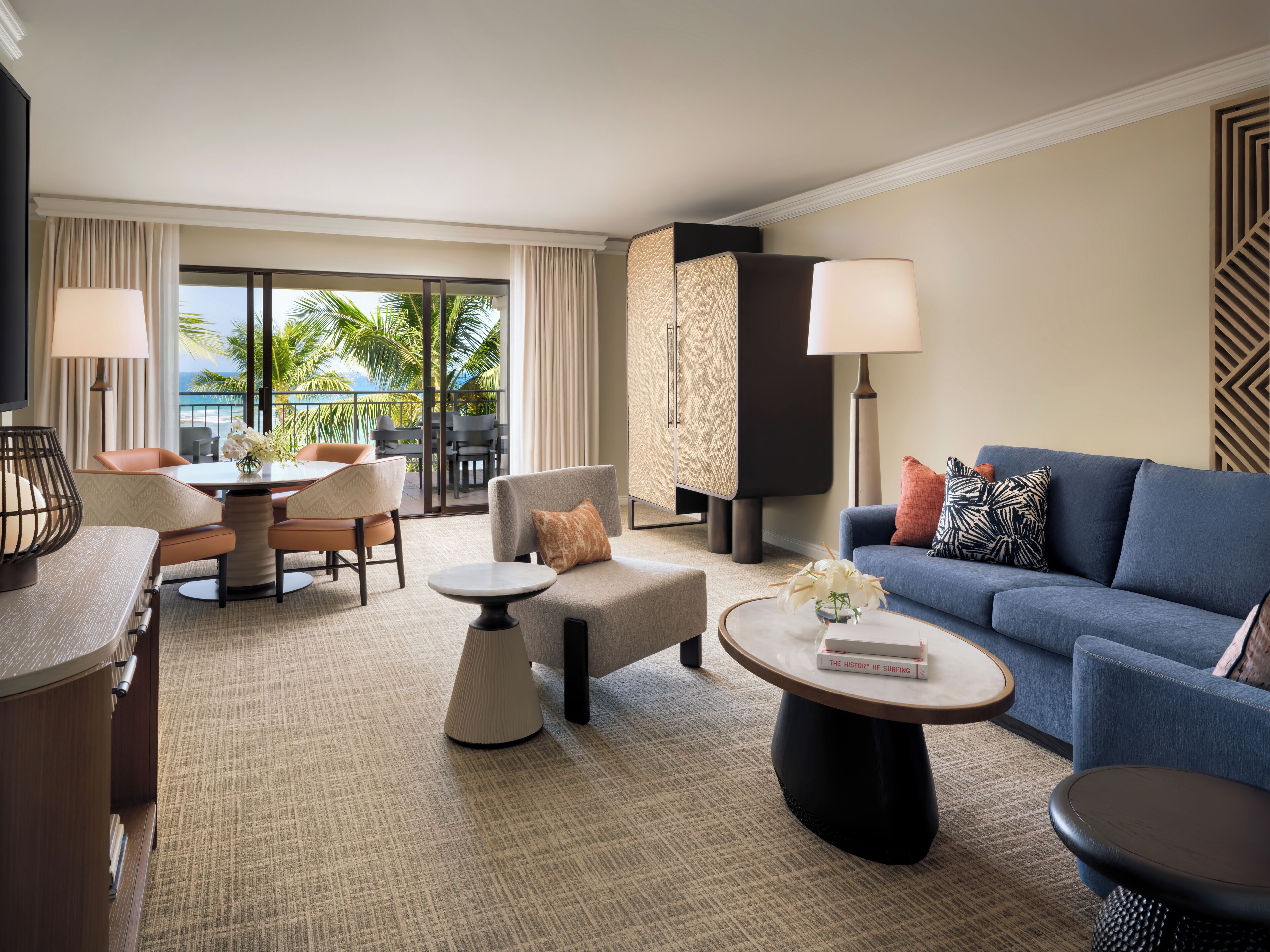 A hotel room with a balcony, a dining area, a sofa, and a coffee table.
