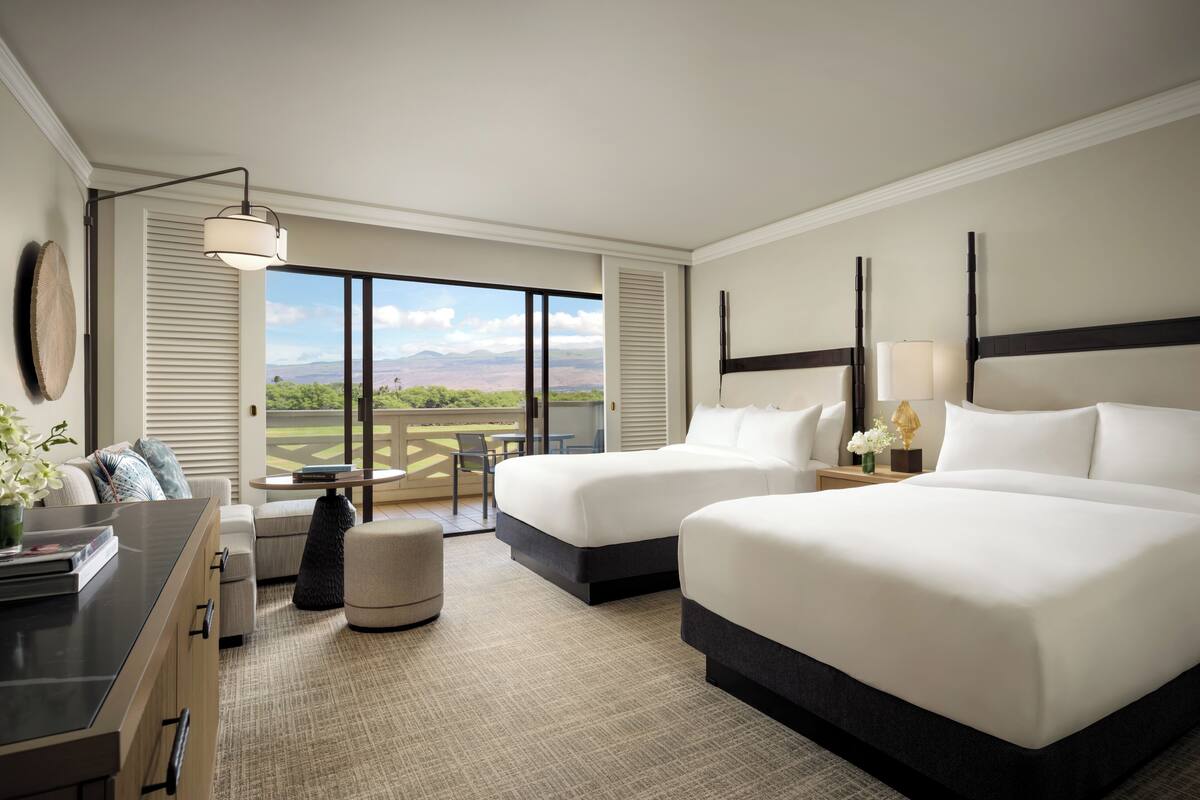 A hotel room with two beds, a desk, a chair, a small table, and a view of the outdoors.
