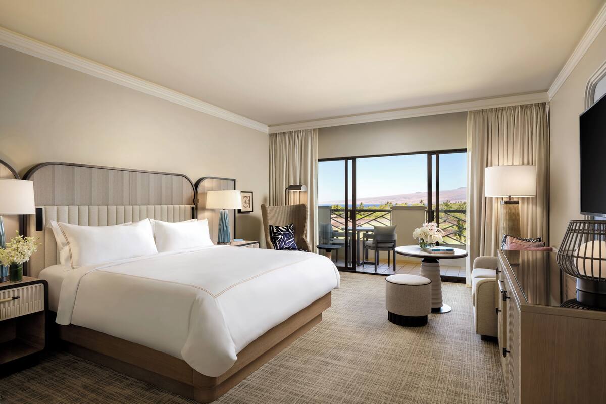 A hotel room with a large bed, a desk, a chair, a small table, and a balcony with a view.