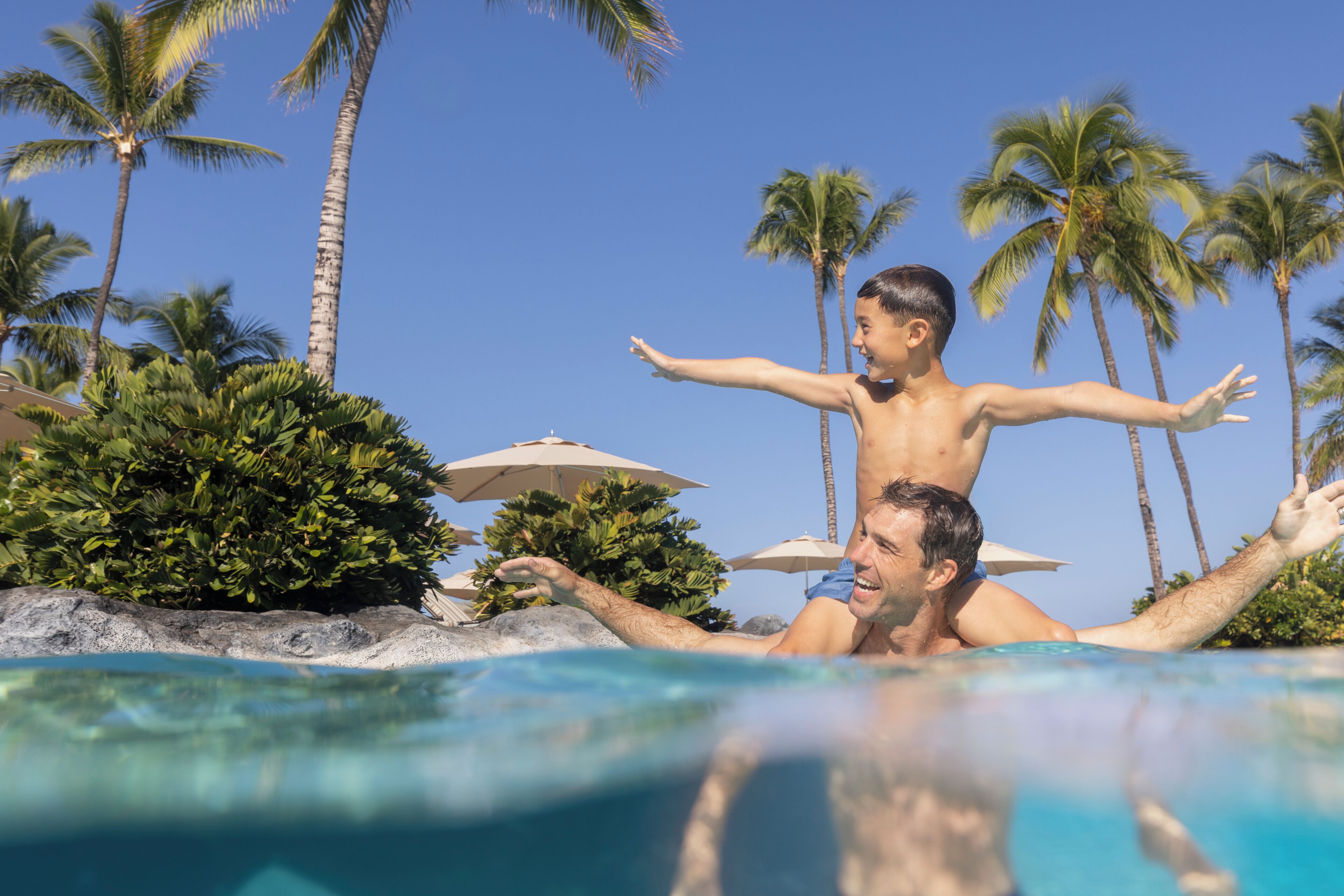 A swimming pool with clear water, surrounded by palm trees and umbrellas.