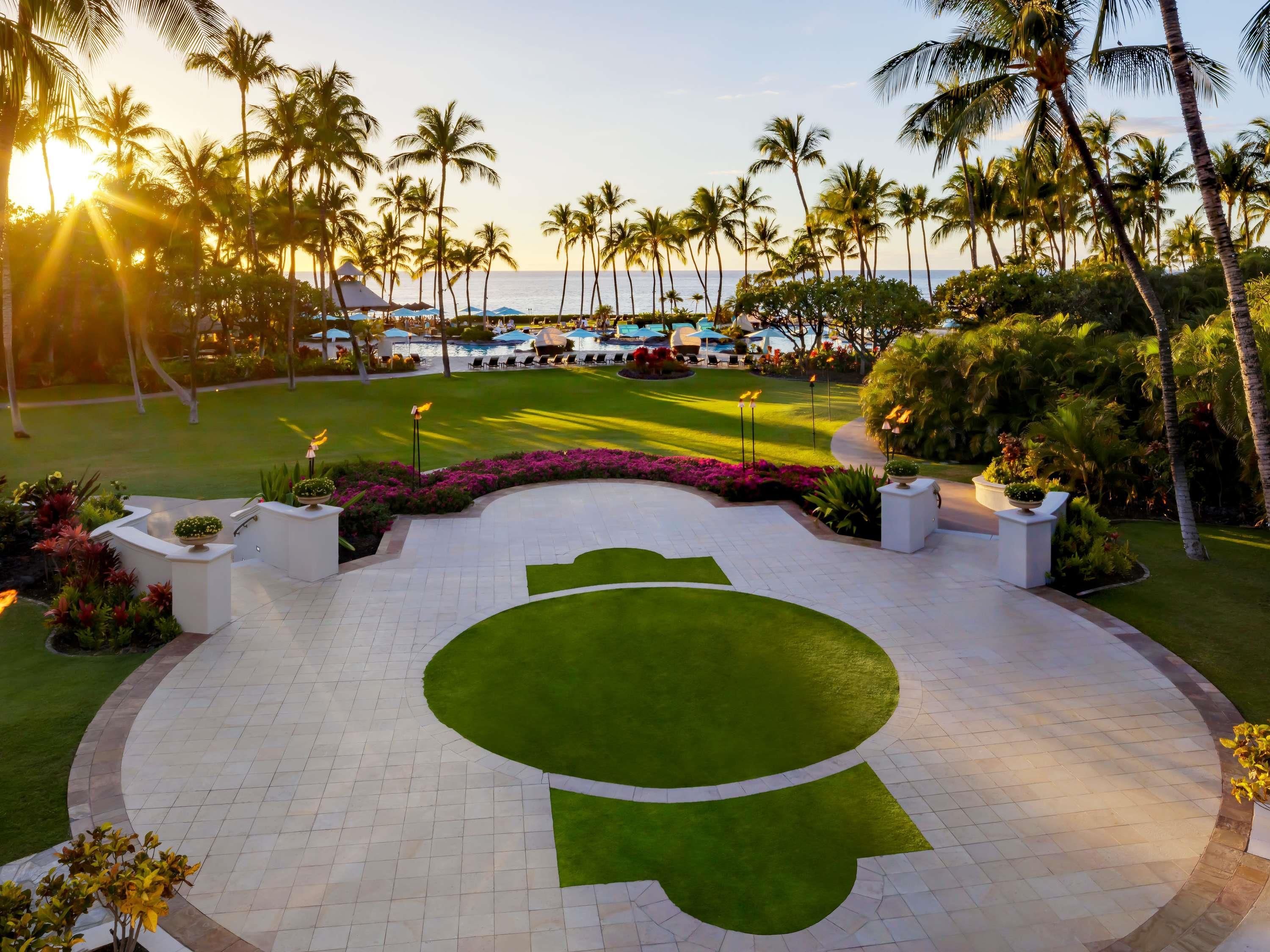 Zona de piscina en un resort con diseño circular, rodeada de palmeras y vista al océano.