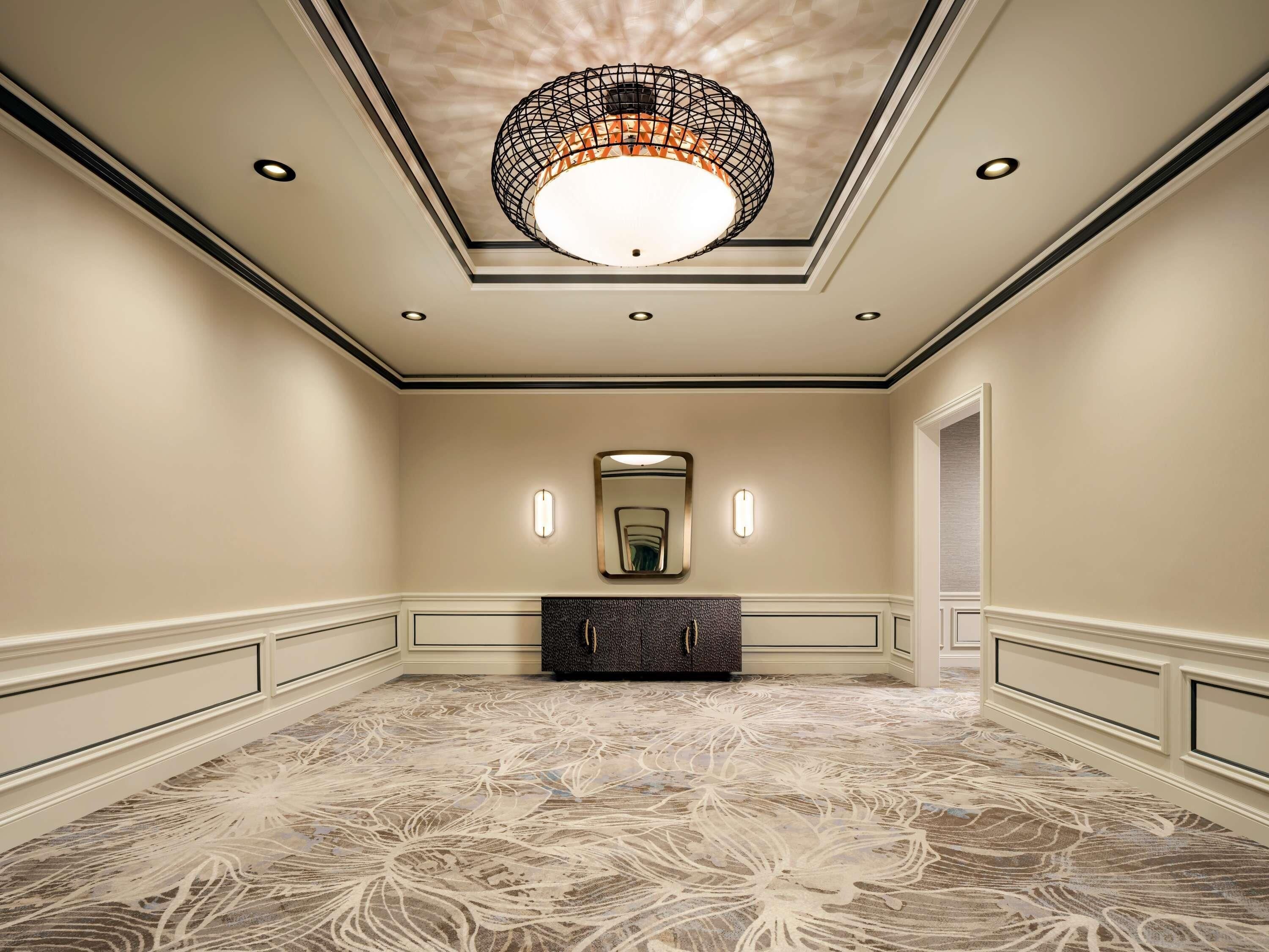 A hotel room with a large mirror, a decorative ceiling light, and a patterned carpet.