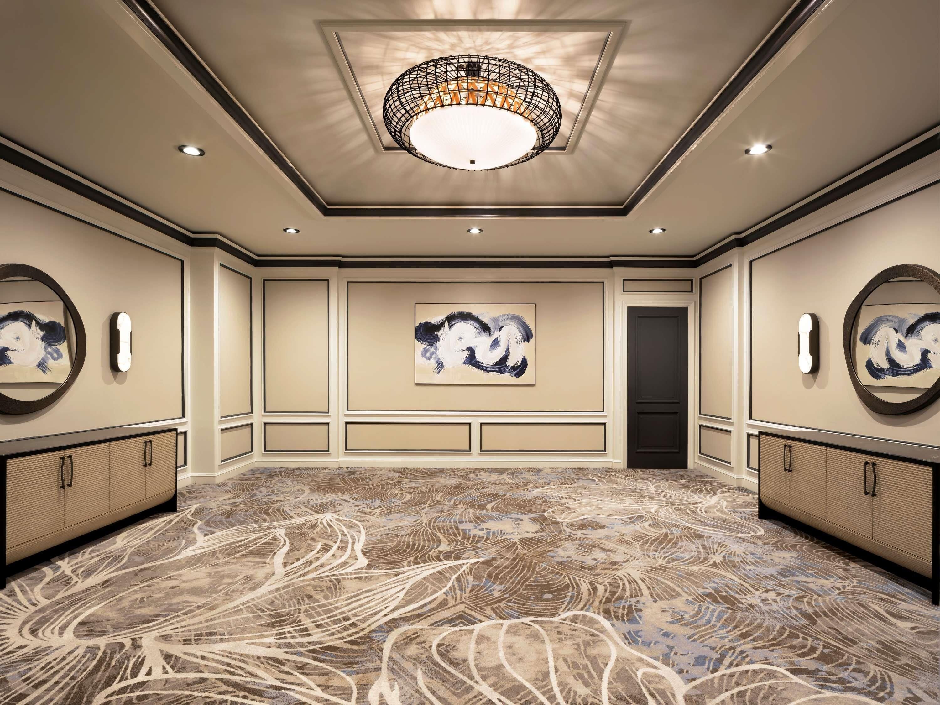 A spacious conference room with a patterned carpet, a central chandelier, and artwork on the walls.