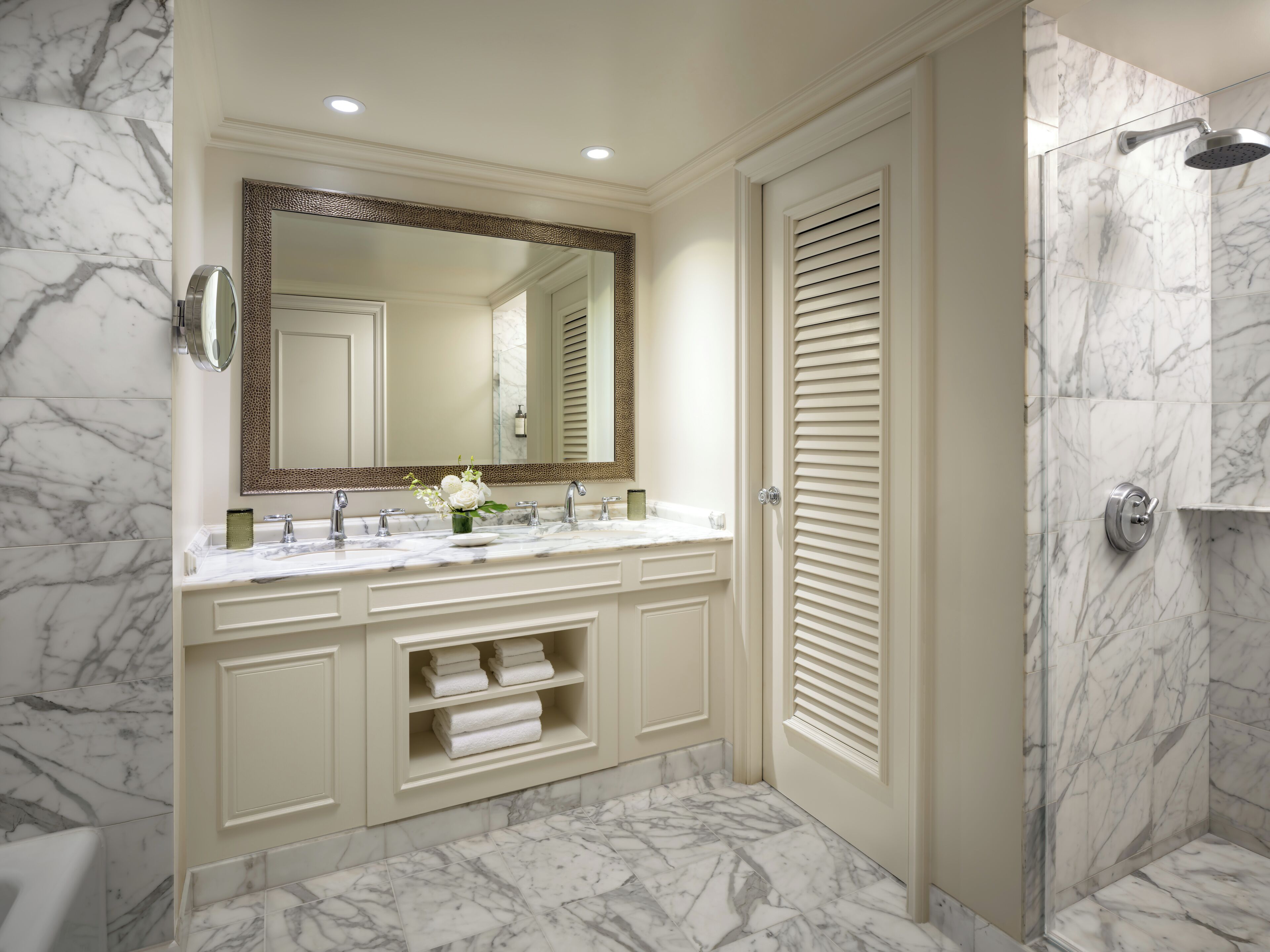 A bathroom with a marble floor, a double sink vanity, a large mirror, and a shower area.