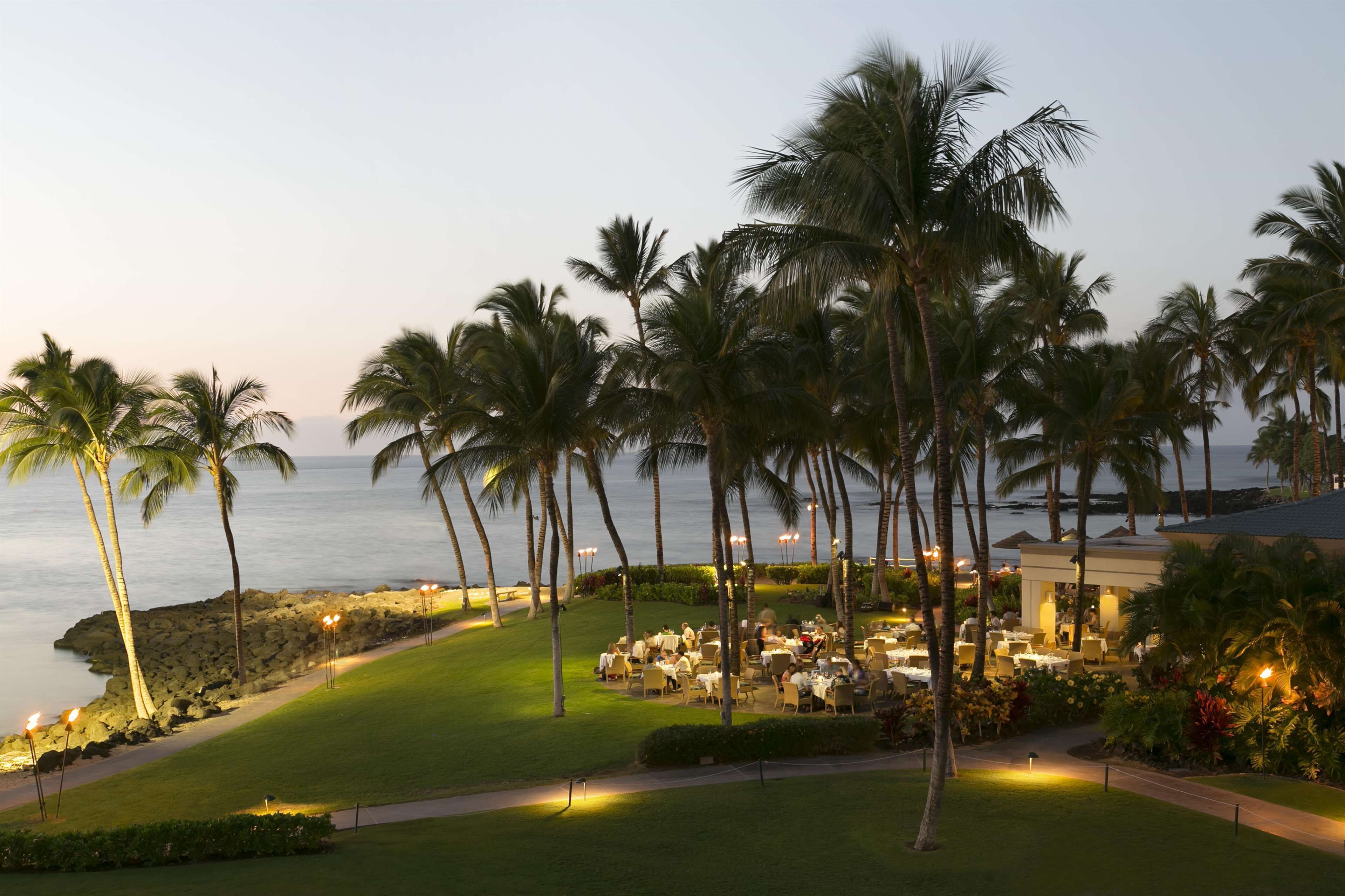 A resort with outdoor dining, palm trees, and a view of the ocean.