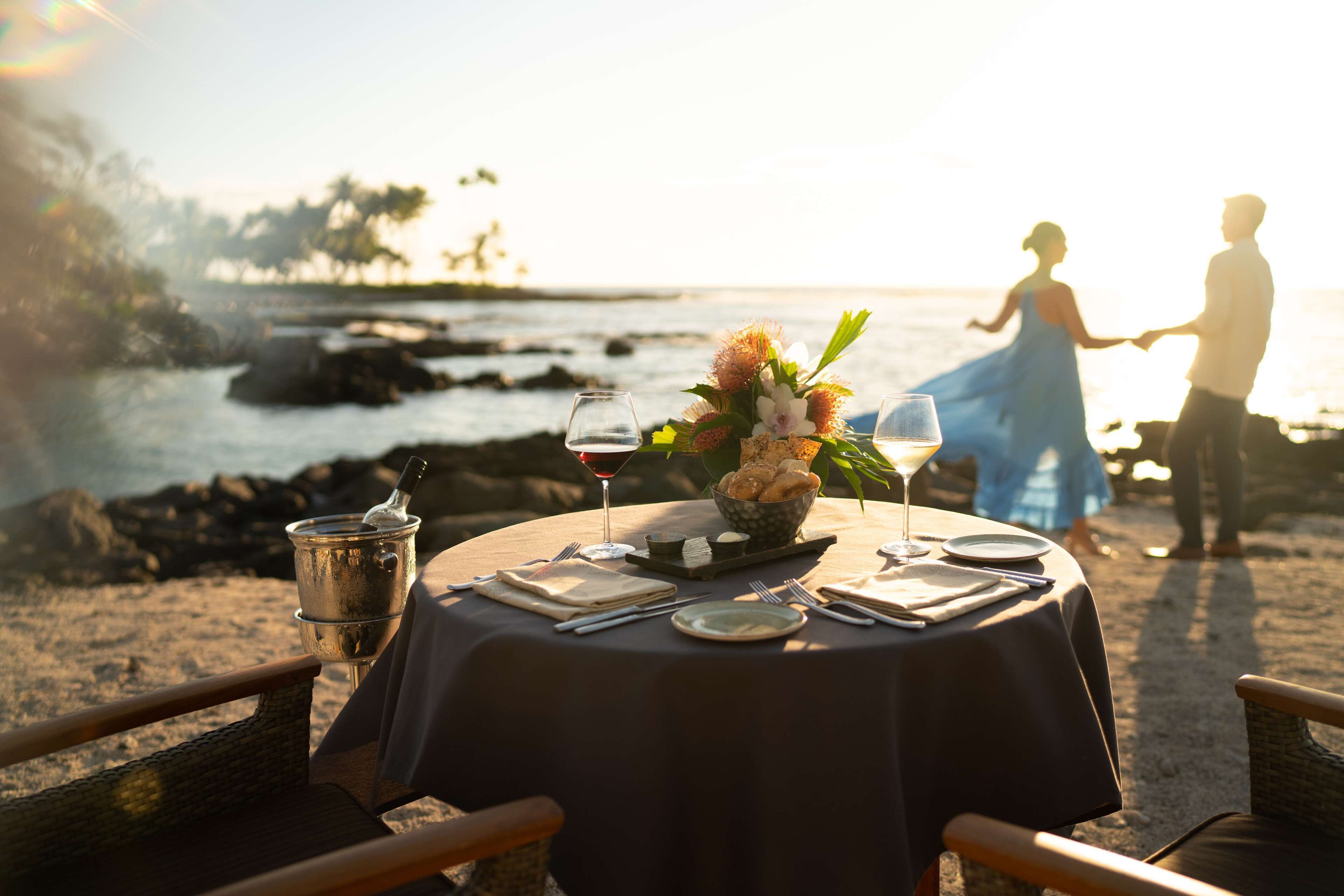 A table set for two with a view of the ocean and a sunset.