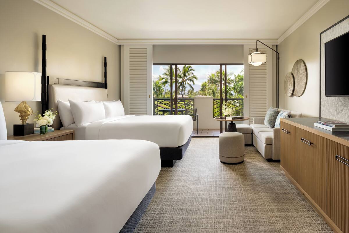 A hotel room with two beds, a desk, a chair, and a TV.