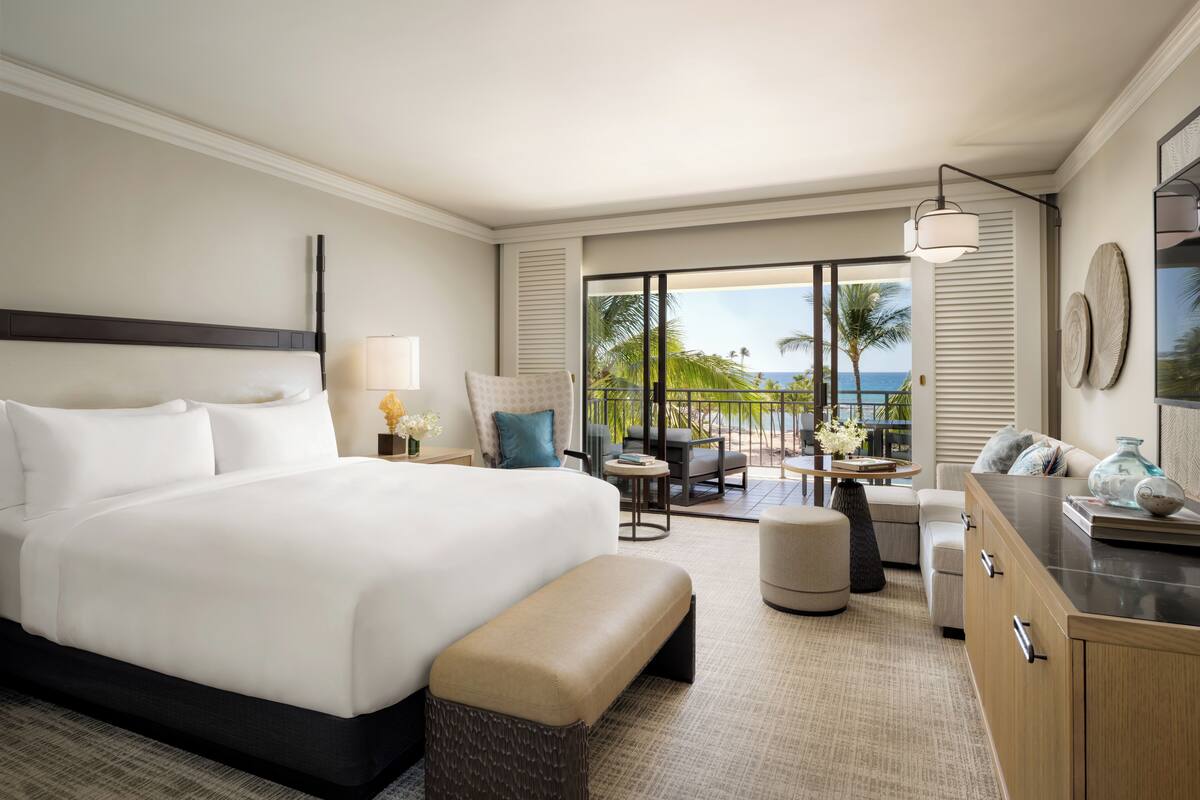 A hotel room with a large bed, a seating area with a view of the beach, and a balcony with a table and chairs.