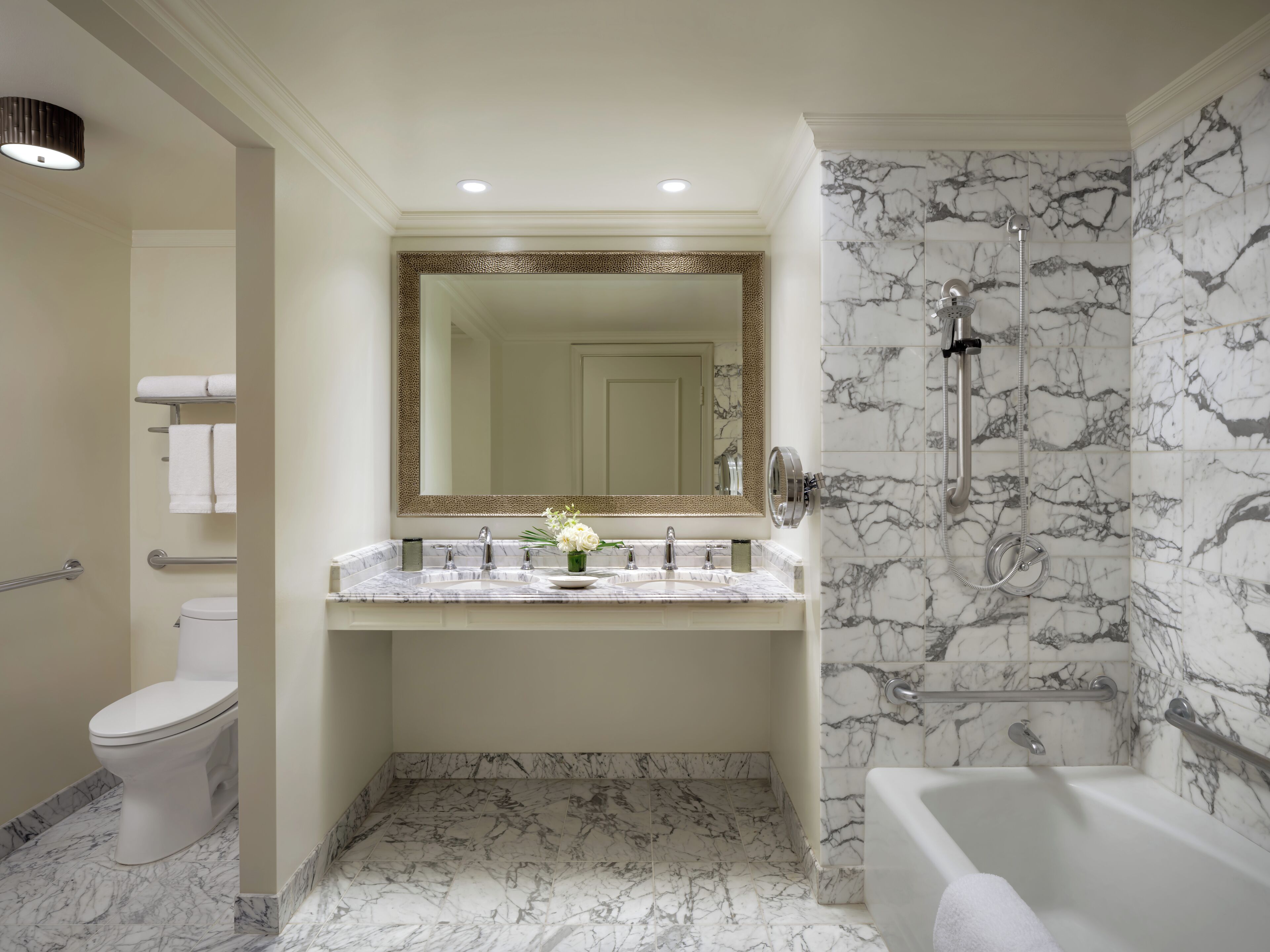 Un bagno con pavimento in marmo, una vasca da bagno, una doccia con soffione manuale, un lavabo con specchio sopra e un water.