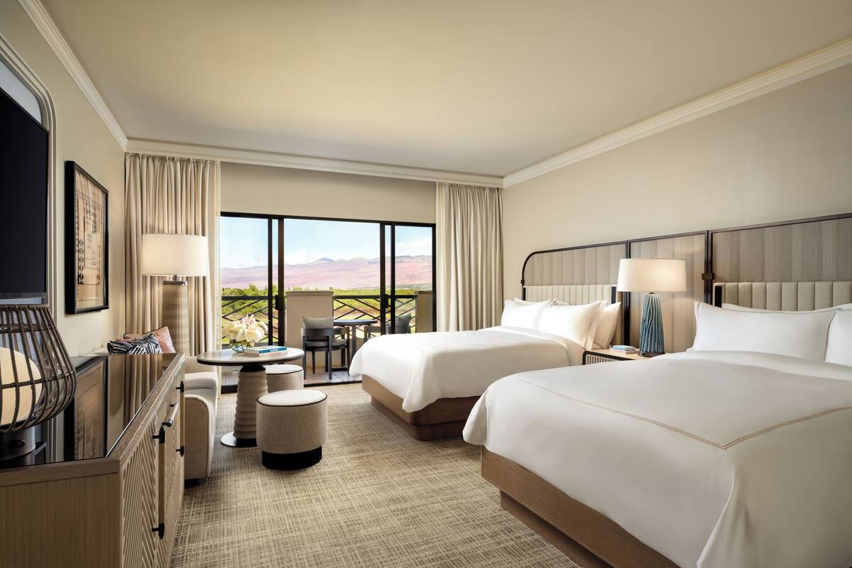A hotel room with two beds, a desk, a chair, a TV, and a view of the mountains.