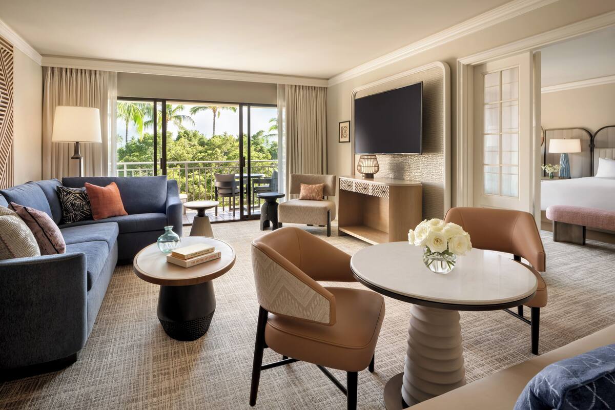 A modern hotel room with a balcony, a large flat-screen TV, a sofa, a coffee table, and a bed.