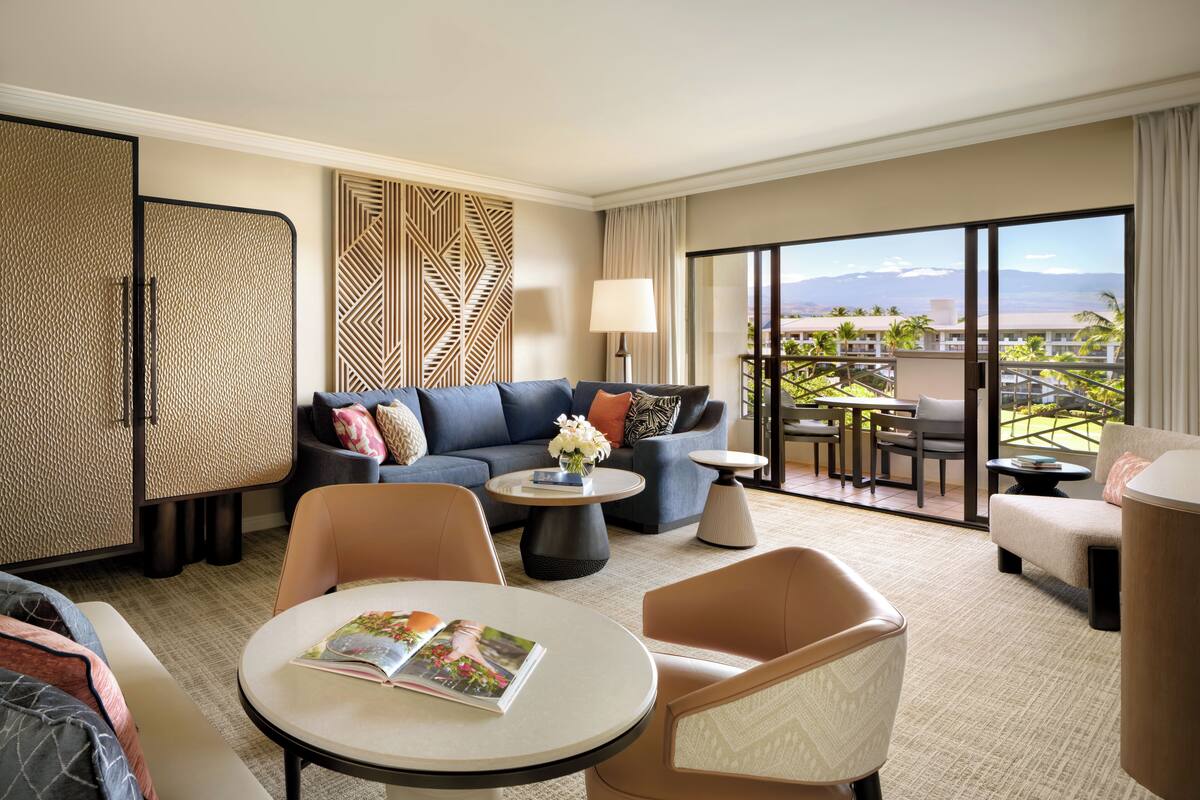 A hotel room with a sofa, armchairs, a coffee table, and a balcony with a view.