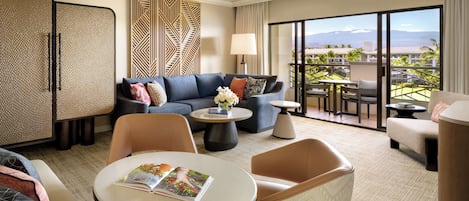 A hotel room with a sofa, armchairs, a coffee table, and a balcony with a view.