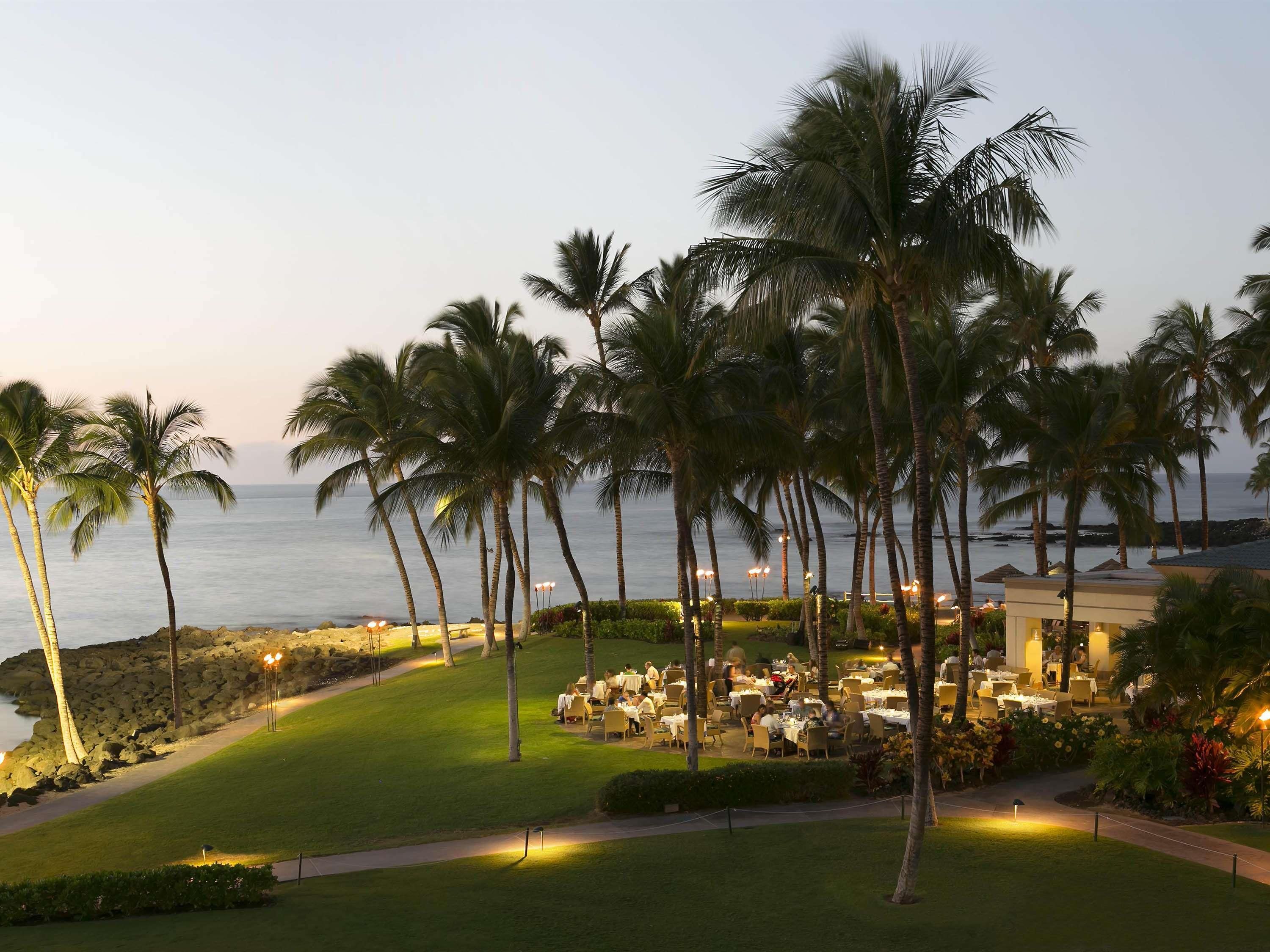 A resort with outdoor dining areas, palm trees, and a view of the ocean.