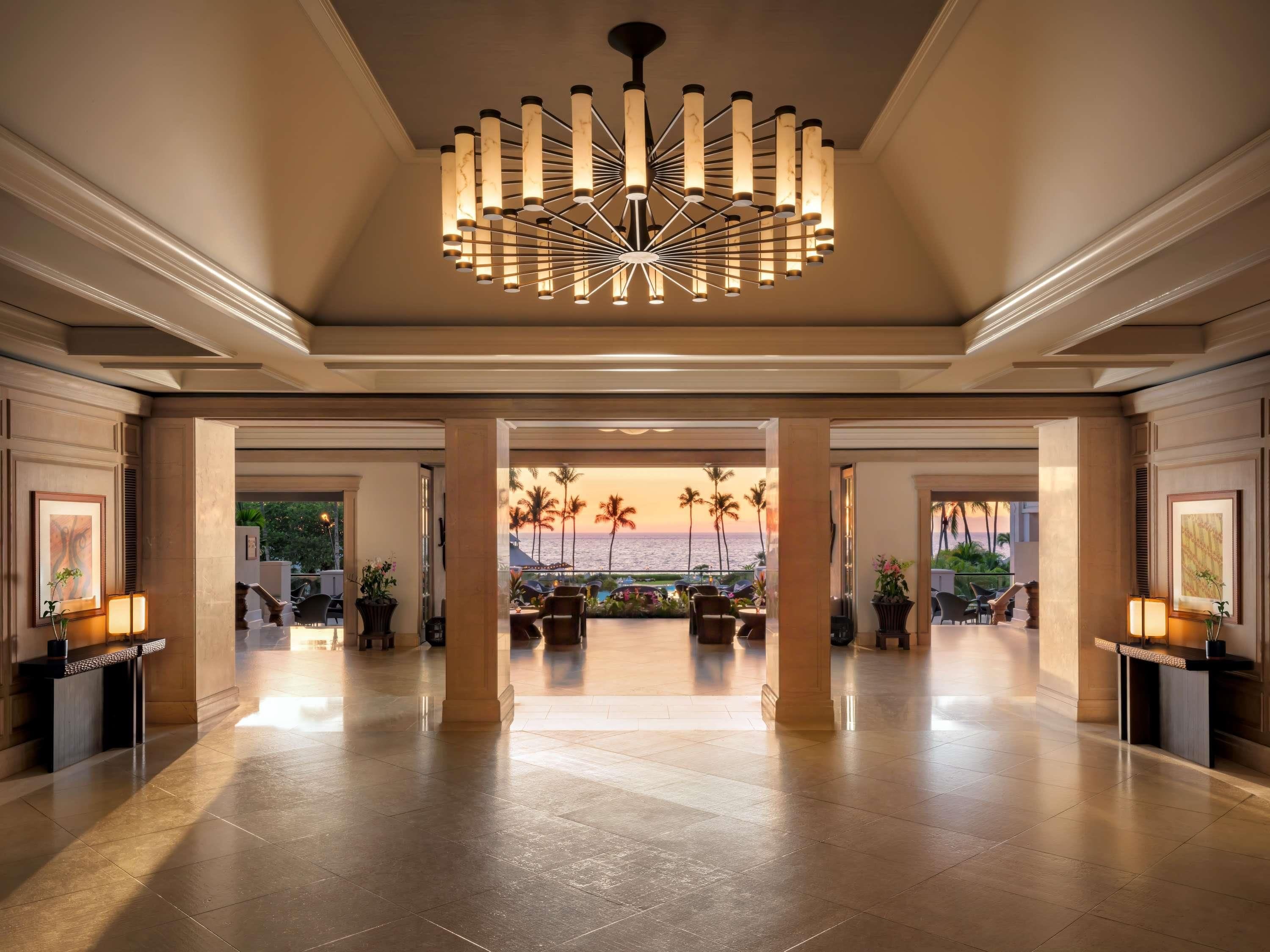 A spacious lobby with a modern chandelier, a view of the ocean, and a reception desk.